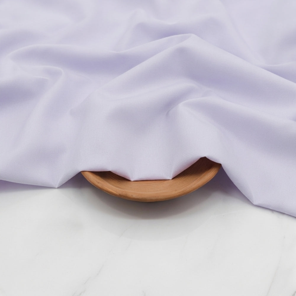 Close-up of light purple fabric draped over a wooden bowl on a white background